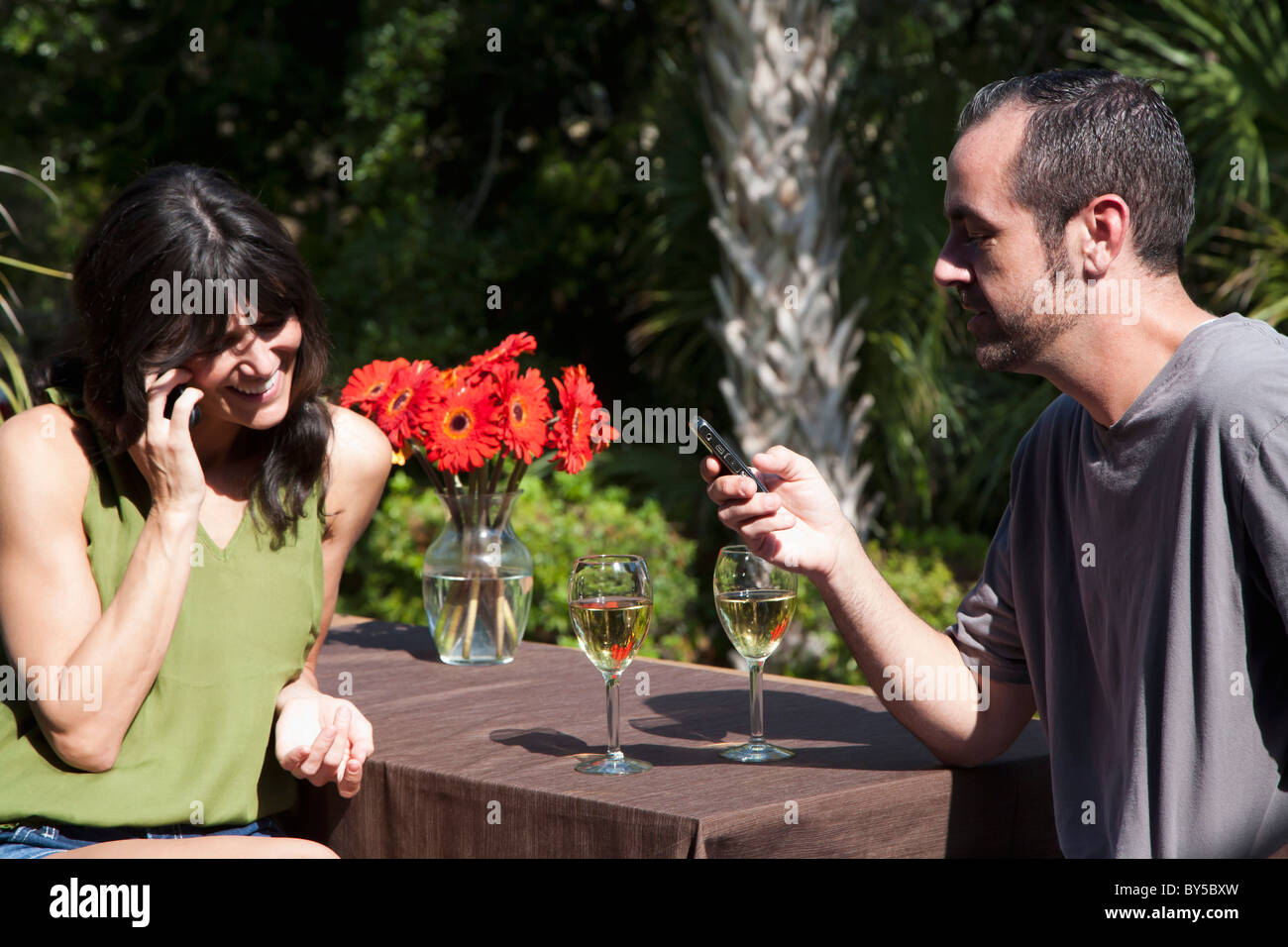 Una donna con il suo mobile mentre il suo fidanzato messaggi di testo su un cortile deck Foto Stock