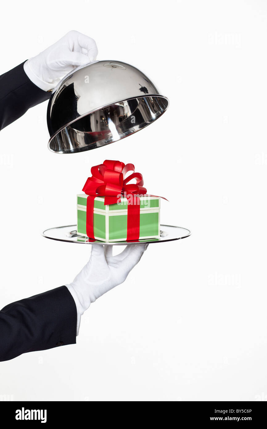 Un maggiordomo tenendo il coperchio off un vassoio a cupola, rivelando un dono, concentrarsi sulle mani Foto Stock