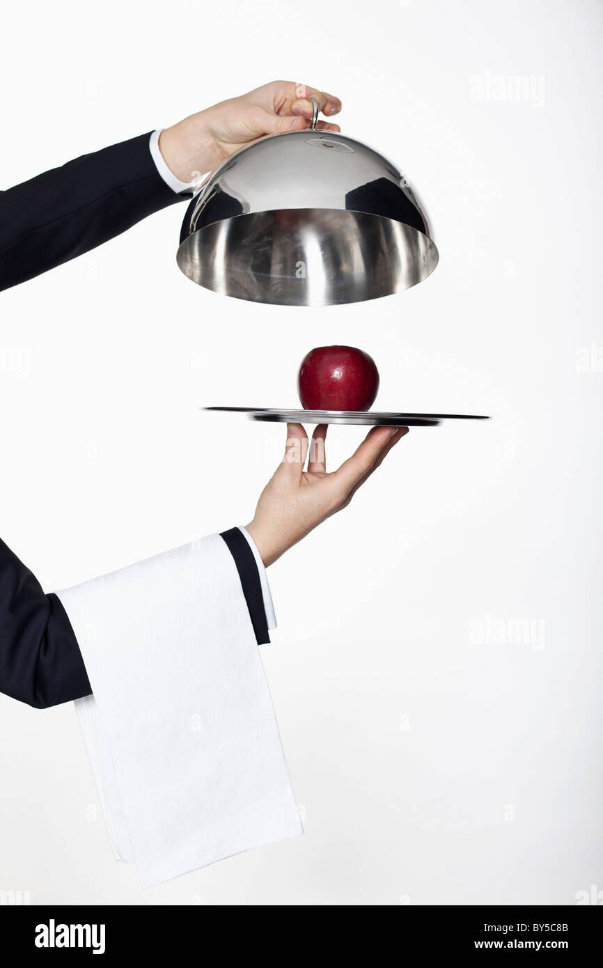 Un maggiordomo tenendo il coperchio off un vassoio a cupola, rivelando una mela rossa, concentrarsi sulle mani Foto Stock