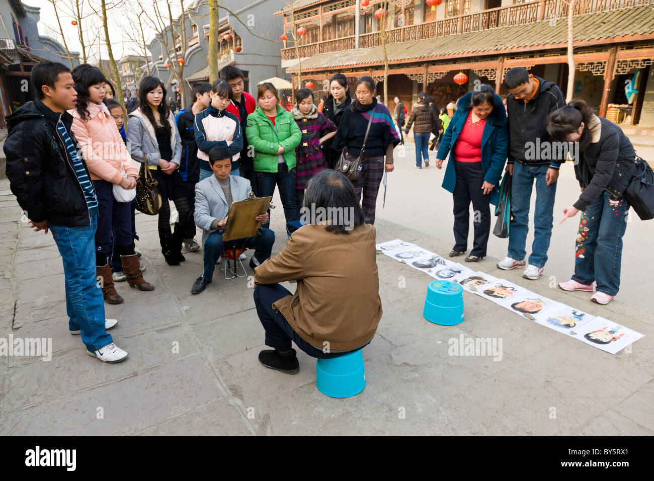 La folla guarda l'artista di strada facendo uno schizzo a matita di un uomo in Huanglongxi, vicino a Chengdu, nella provincia di Sichuan, in Cina. JMH4352 Foto Stock