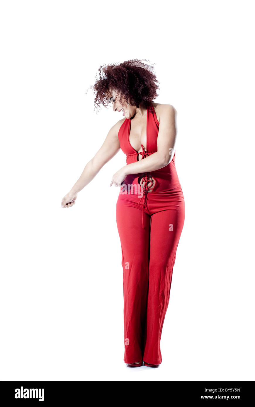 La donna brasiliana ballando e giocando in studio. La donna indossa un abito rosso e capelli ricci Foto Stock