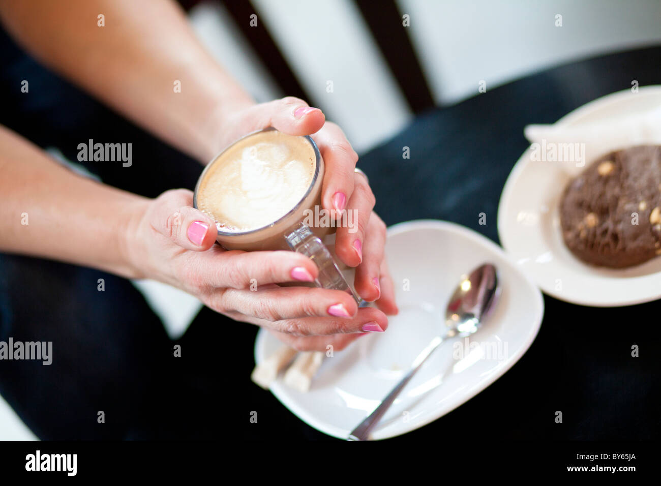 Una donna di mano afferra un caffelatte bevanda caffè accanto a un cookie al cioccolato biscotto. Foto Stock Una donna di mano afferra un caffelatte bevanda caffè accanto a un cookie al cioccolato biscotto. Foto Stock