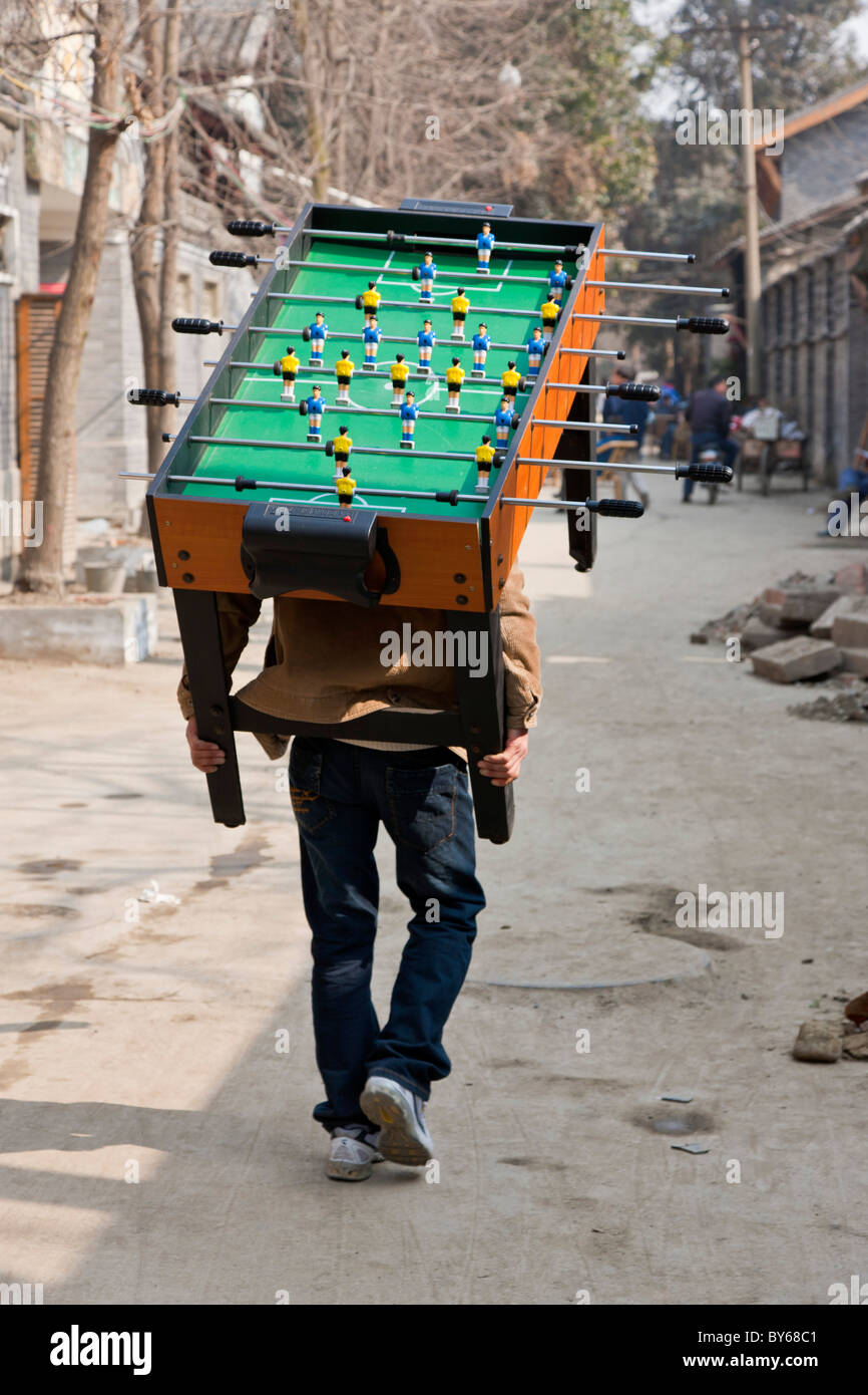 Uomo che porta Subbuteo® football soccer tavolo da gioco sul suo retro attraverso l'Hutong, Chengdu nella provincia di Sichuan, in Cina. JMH4408 Foto Stock