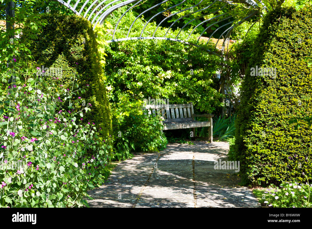 Sedile in legno o banco in un angolo ombreggiato sotto una pergola in un paese di lingua inglese giardino d'estate. Foto Stock