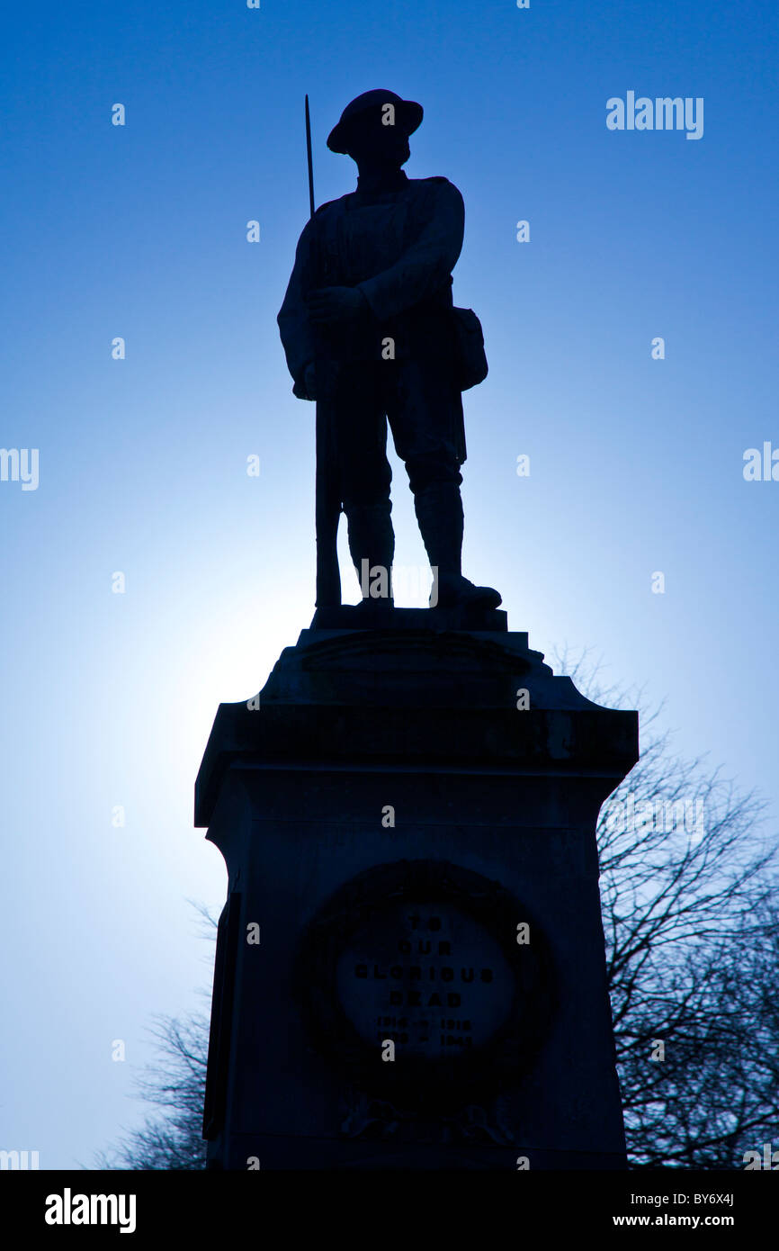 Monumento ai caduti in guerra con una statua di un soldato stagliano contro il sole invernale in Trowbridge Park, Wiltshire, Inghilterra, Regno Unito Foto Stock