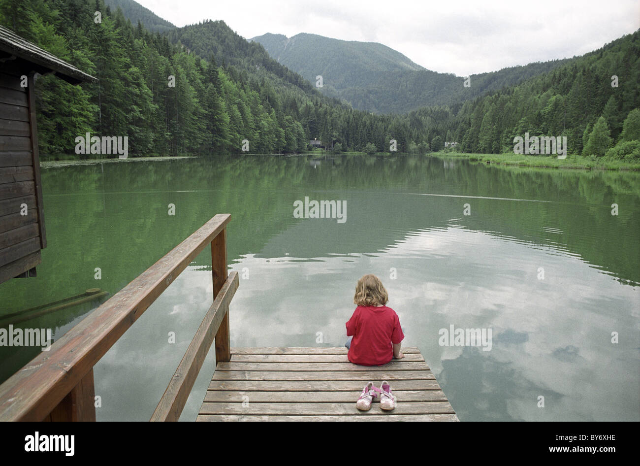 Una piccola ragazza seduta da un lago, Schaffner Weiher, Stodertal, Austria, Alpi, Europa Foto Stock