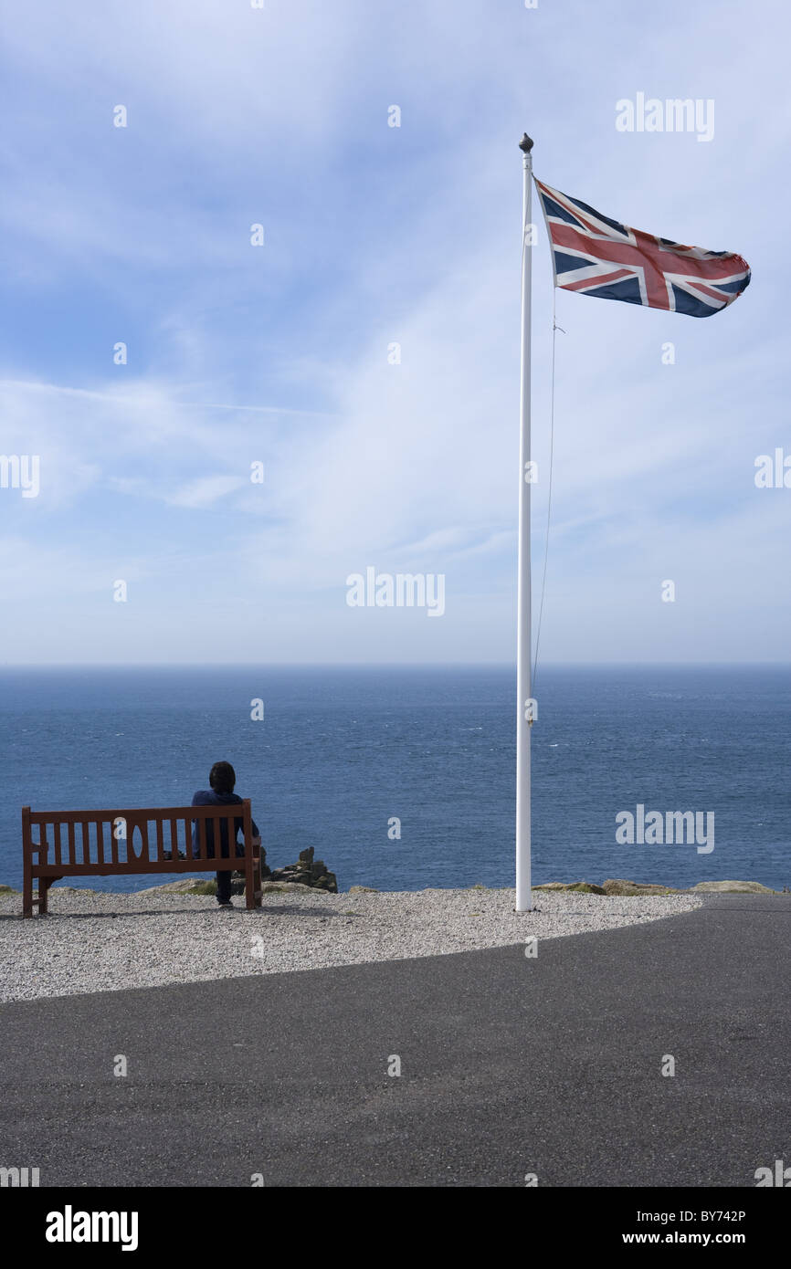 Donna sul banco e Union Jack bandiera britannica a bandiera pole, Land's End, Cornwall, Inghilterra, Europa Foto Stock
