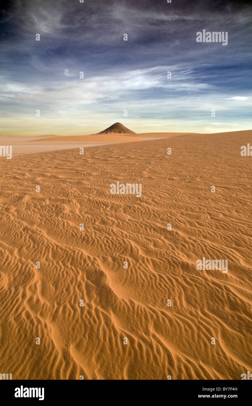 Una formazione rocciosa vulcanica a forma di cono si stende dalla sabbia nella regione di Gilf Kebir del deserto occidentale (Sahara) dell'Egitto. Foto Stock