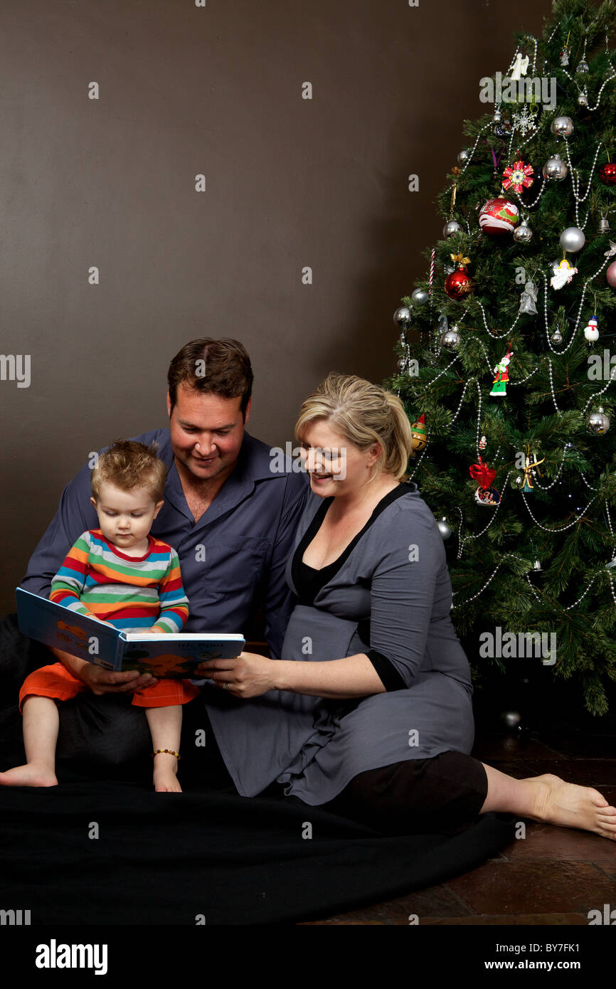 La famiglia felice la lettura di un libro per bambini insieme al tempo di Natale con il loro bambino figlio in modo che egli possa godere di lettura Foto Stock