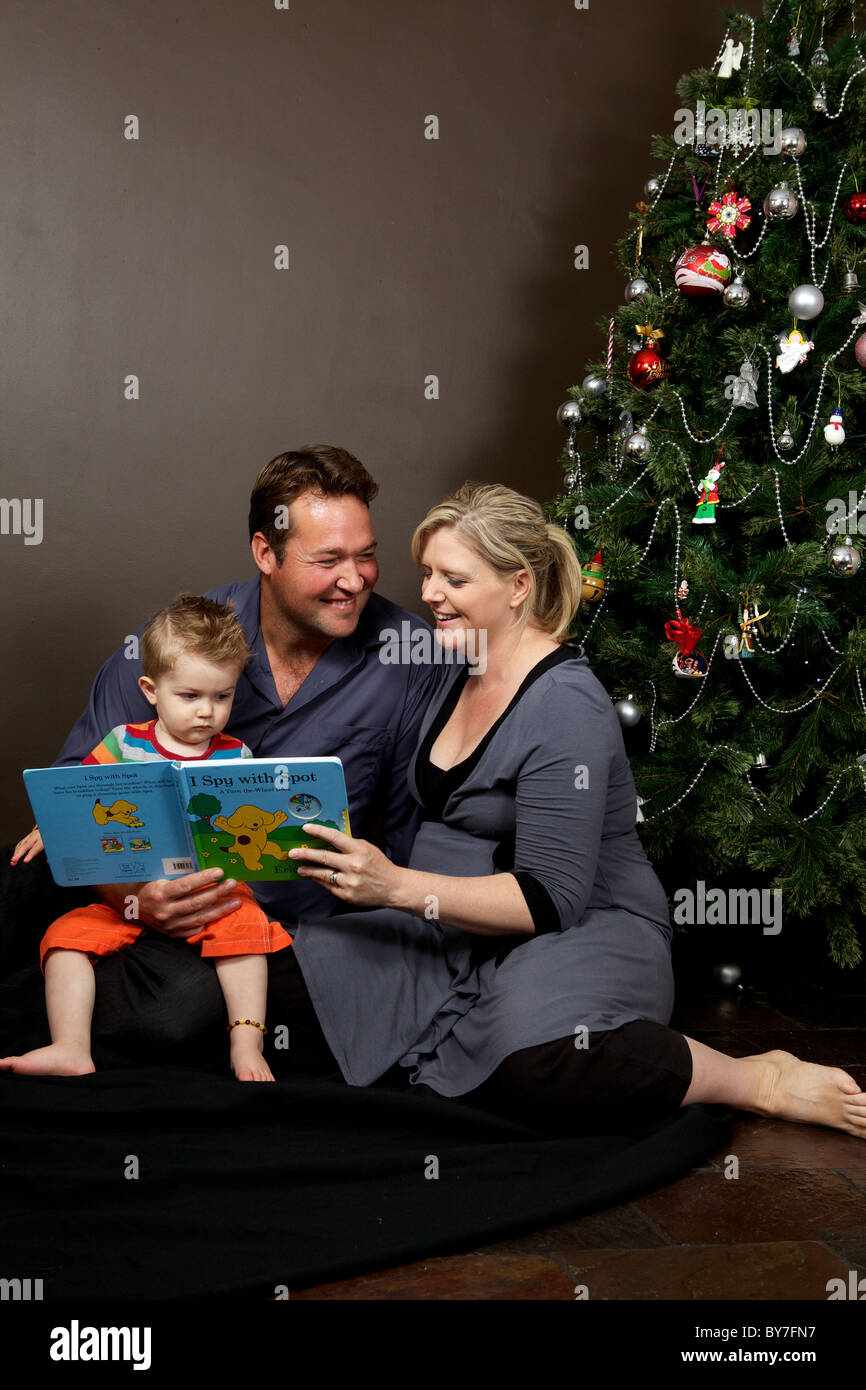 Il padre e la madre la lettura al loro bambino figlio insieme con l'albero di Natale, famiglia felice Foto Stock