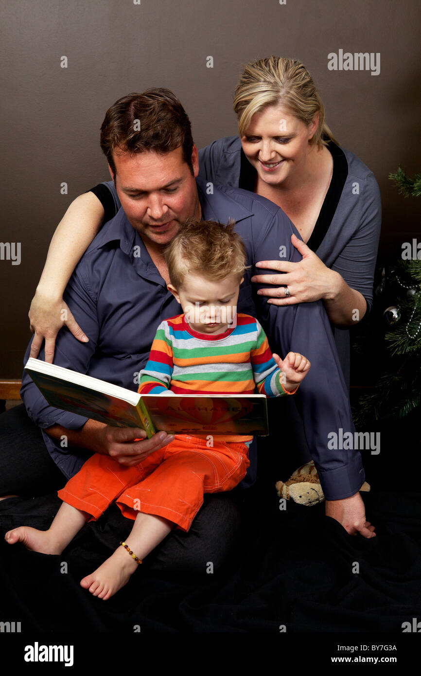 La famiglia felice la lettura di un libro per bambini insieme al tempo di Natale con il loro bambino figlio in modo che egli possa godere di lettura Foto Stock