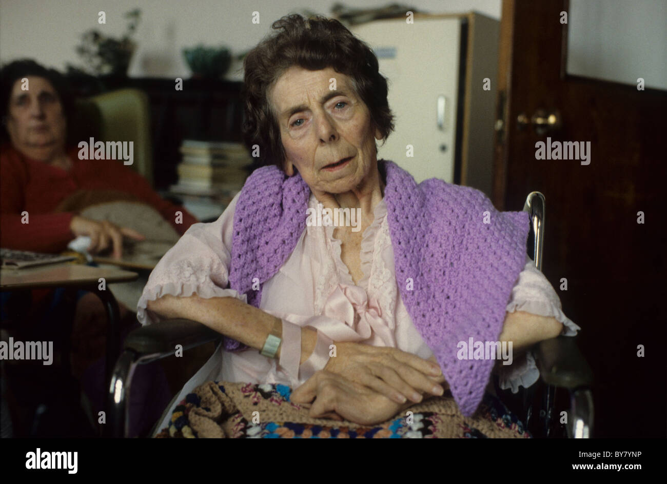 Una paziente anziana che guarda alla macchina fotografica che indossa un viola scialle malvetto seduto accanto al suo comodino in un Reparto ospedaliero in Galles Regno Unito KATHY DEWITT Foto Stock