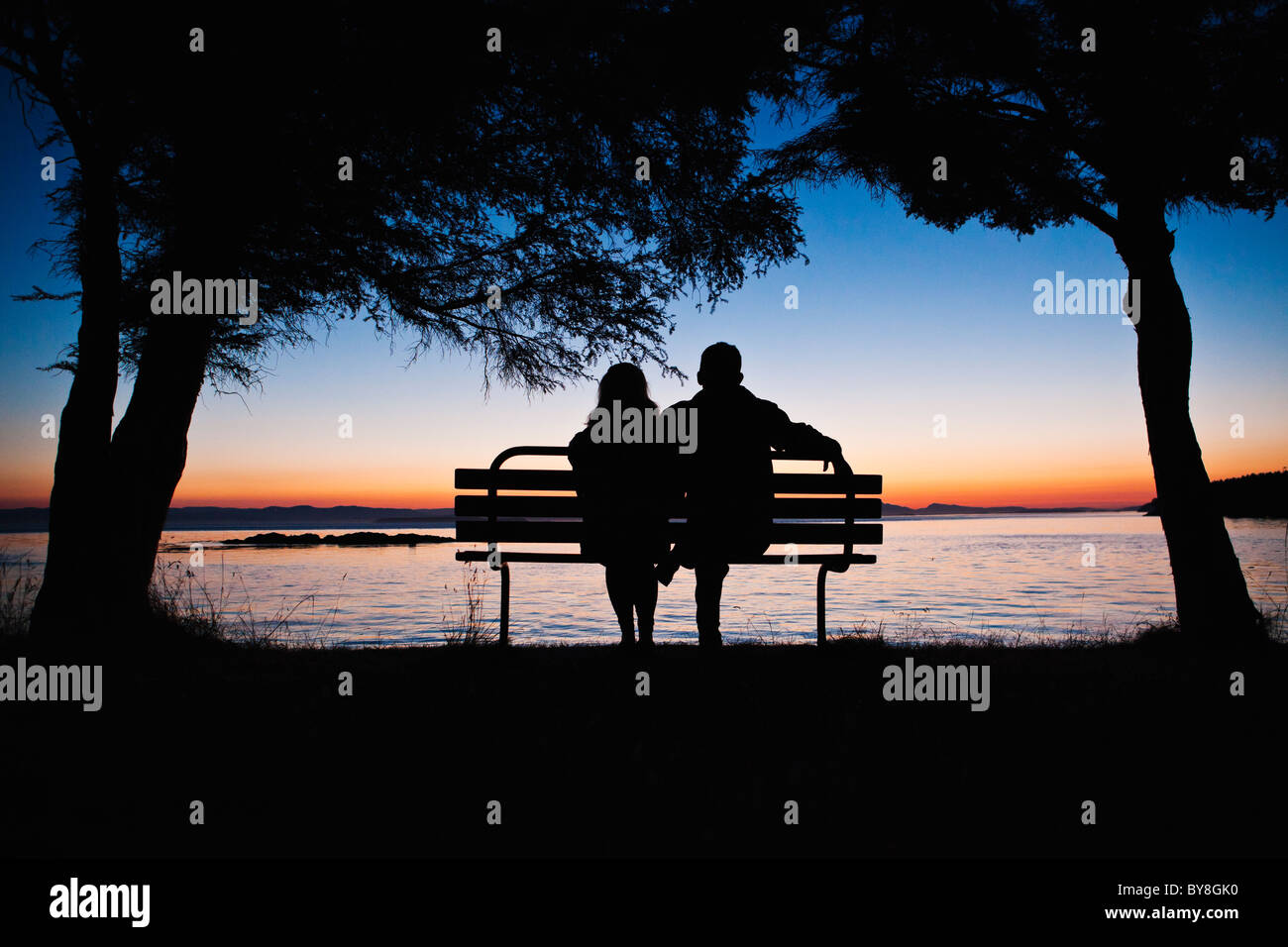 Un uomo e una donna baciare su una panchina nel parco al tramonto. Parcheggio contea di San Juan Island, Washington, Stati Uniti d'America. Foto Stock