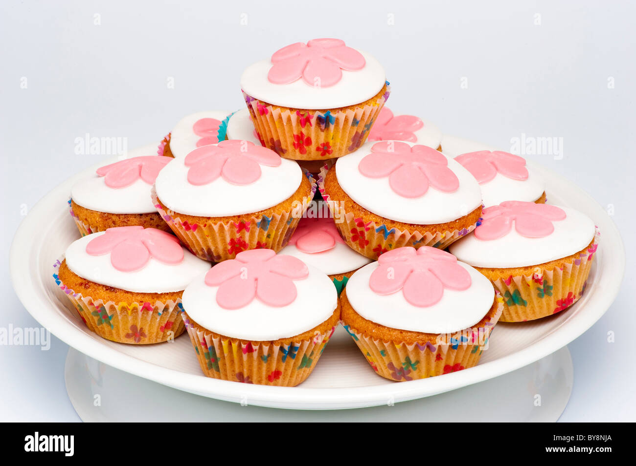 Pila di piccoli cupcakes, noti anche come panini, con glassa bianca decorata con fiori rosa fondente. Foto Stock