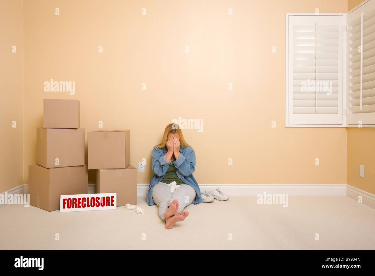 Turbare la donna con tessuti sul pavimento accanto alle caselle di preclusione e Real Estate Sign in stanza vuota. Foto Stock