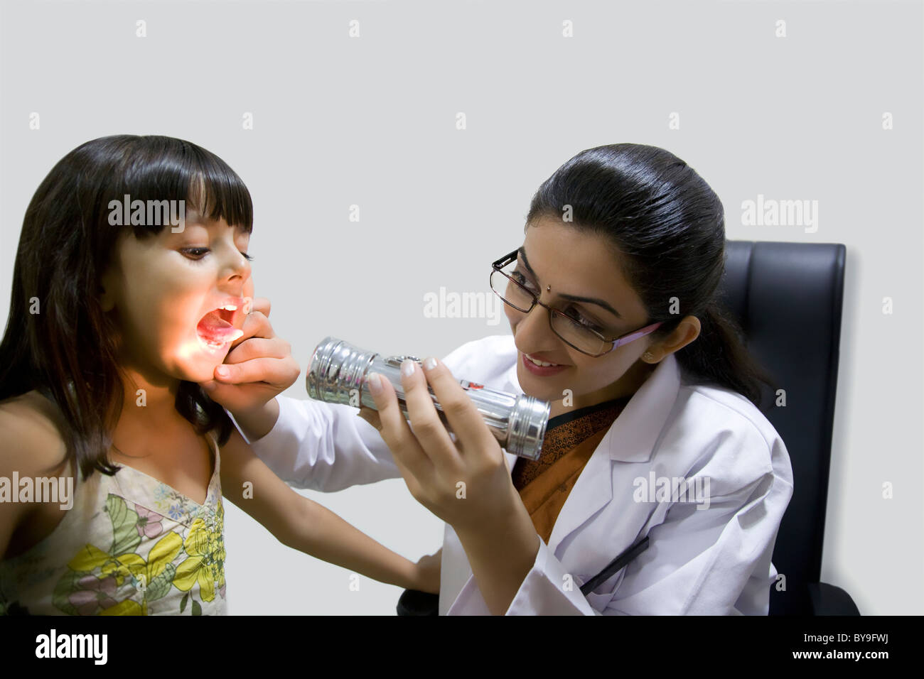 Medico cerca all'interno di una bocca di ragazze con una torcia Foto Stock