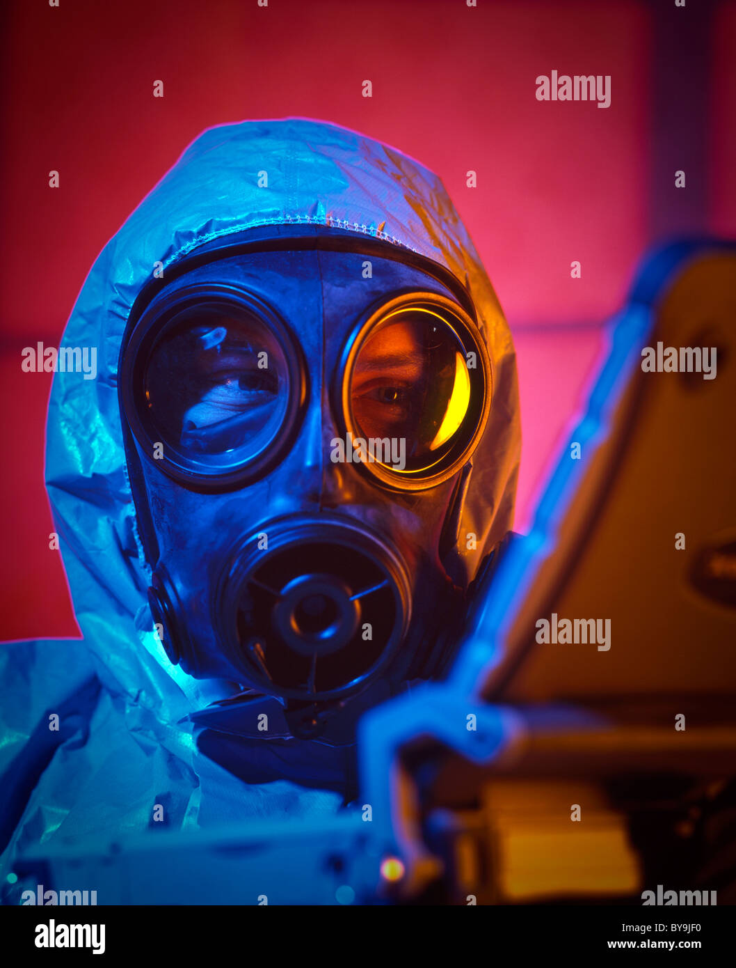Uomo che indossa una faccia maschera a gas vestito in una guerra chimica suit usando un computer portatile Foto Stock
