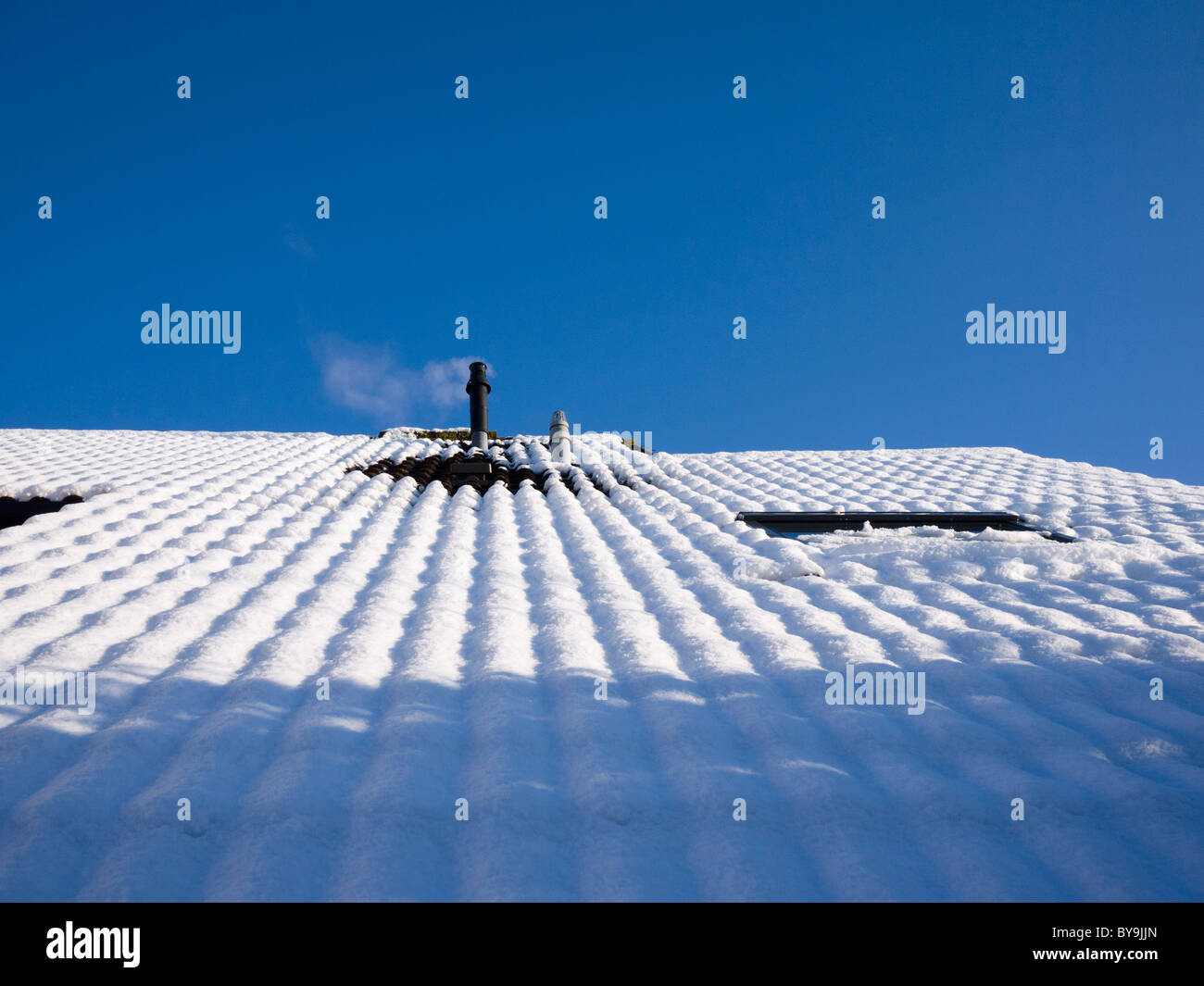 Una combinazione interno canna fumaria caldaia su un tetto emettendo vapore su una coperta di neve tetto contro un cielo blu chiaro. Foto Stock