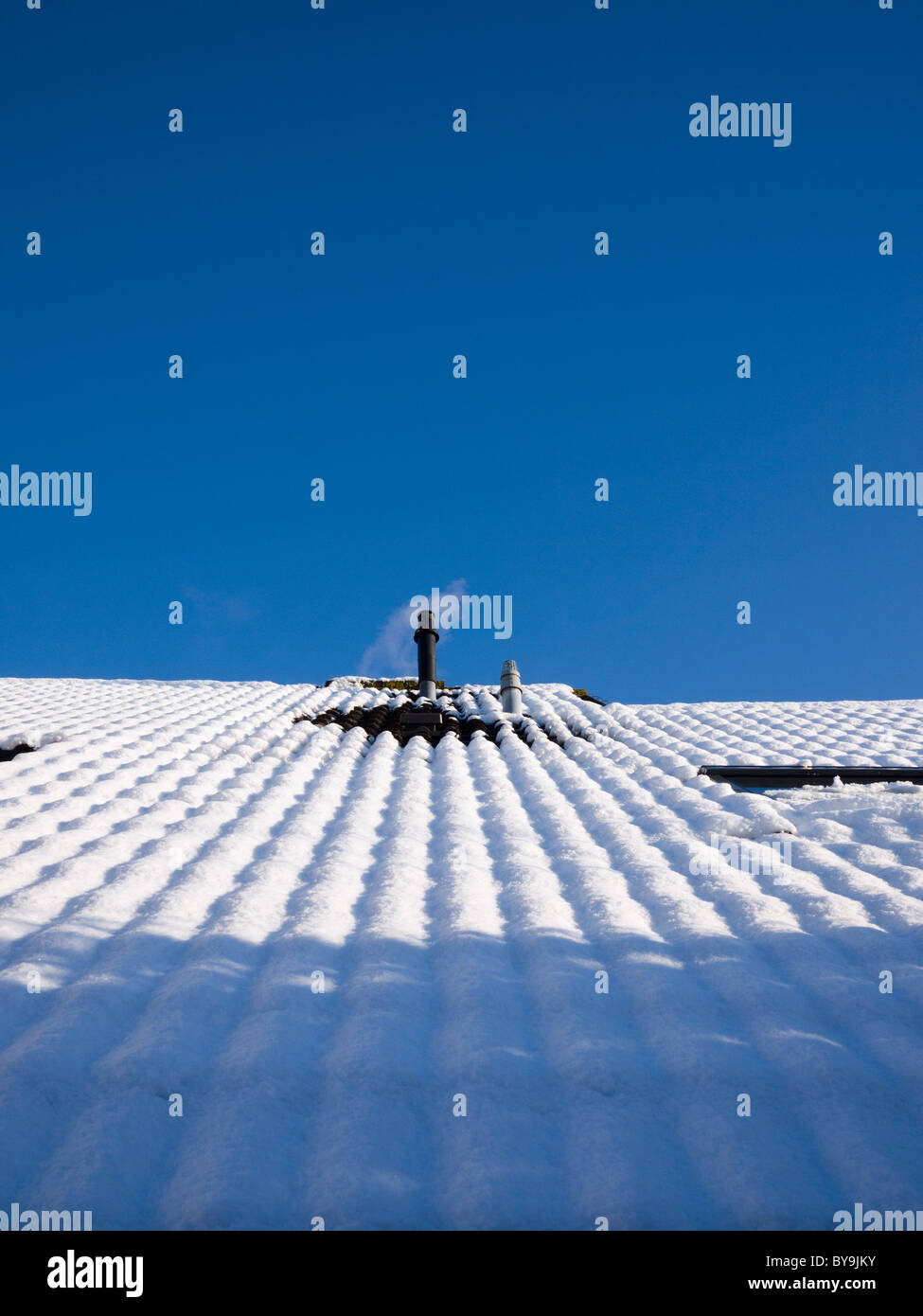 Una combinazione interno canna fumaria caldaia su un tetto emettendo vapore su una coperta di neve tetto contro un cielo blu chiaro. Foto Stock