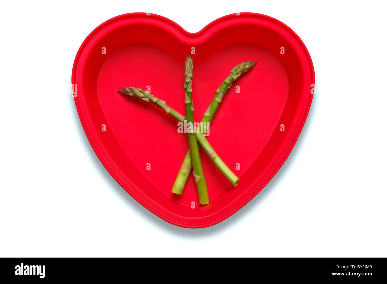Foto concettuale di asparagi in un cuore piatto sagomato per rappresentare un amore del vegetale, isolato su sfondo bianco Foto Stock