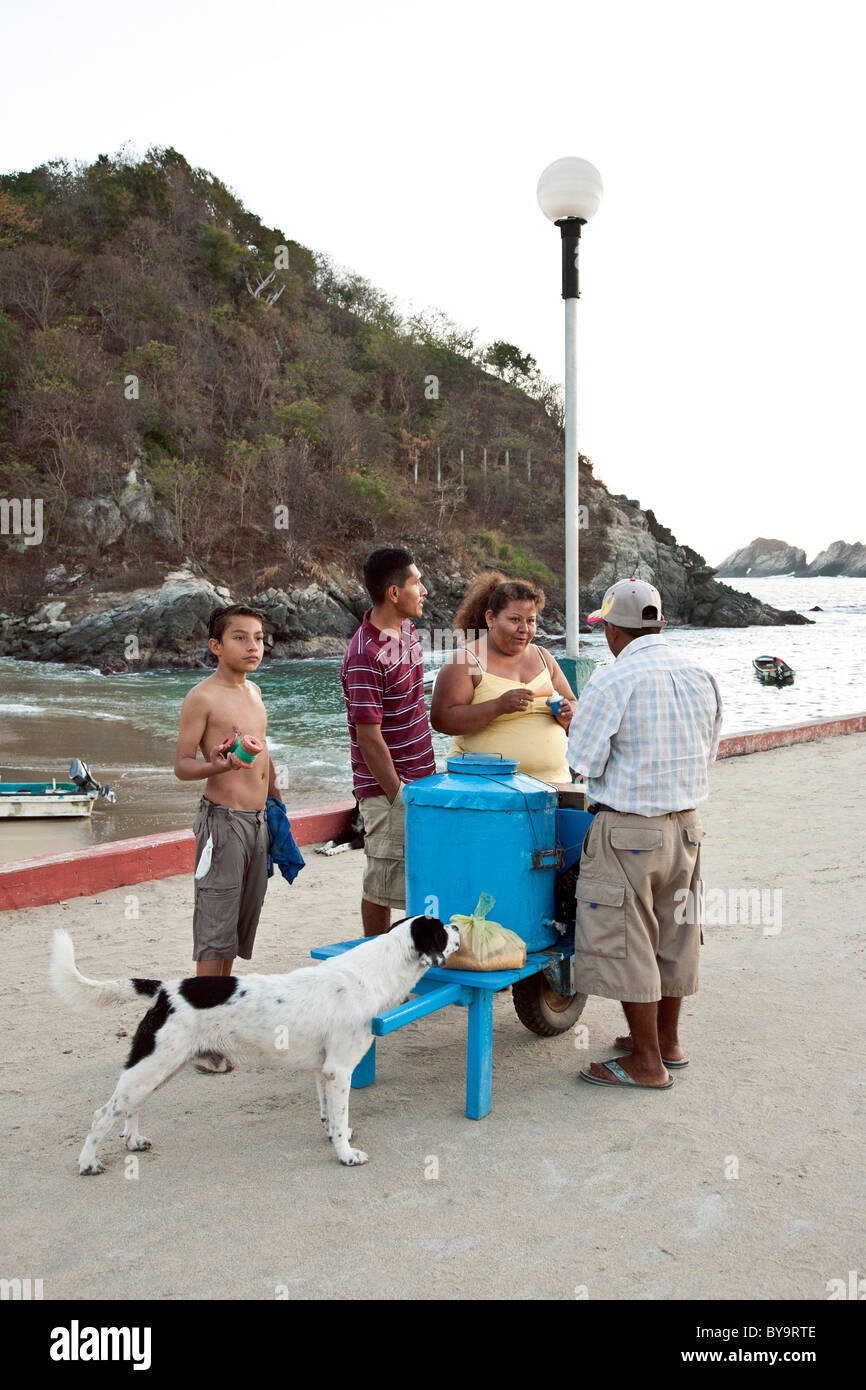 Ice Cream vendor serve clienti in serata da un blu brillante fatto a mano carrello sul molo a Puerto Angel dello Stato di Oaxaca Messico Foto Stock