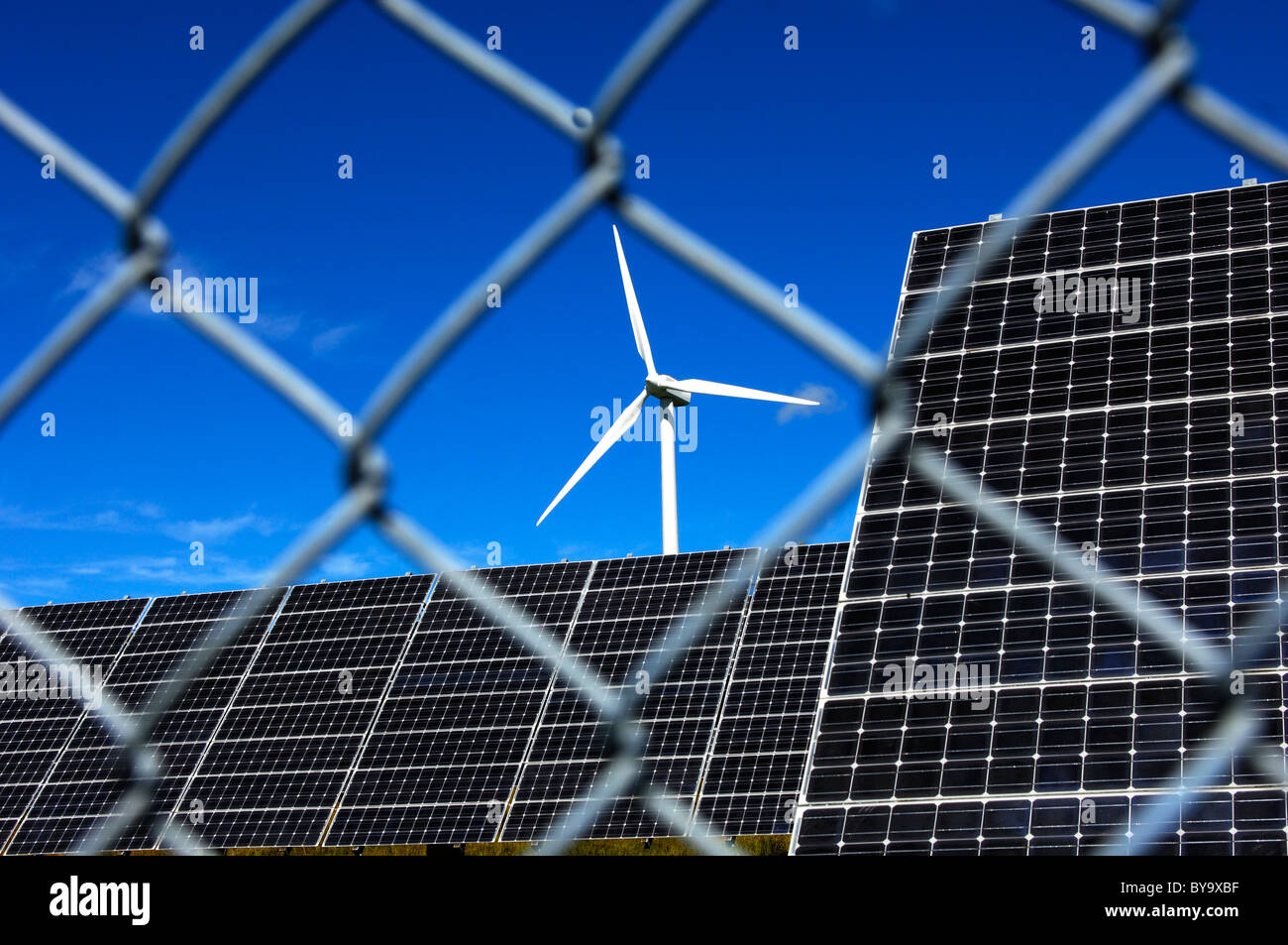 Pannelli solari e una turbina a vento dietro un ingranamento recinto di sicurezza, energia solare stazione Mont Soleil, Giura, Svizzera Foto Stock