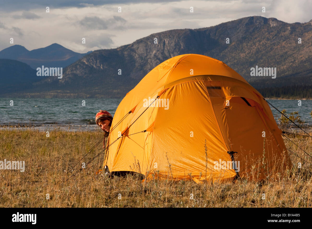 Giovane donna che guarda fuori di una tenda, Kusawa lago, le montagne alle spalle, Yukon Territory, Canada Foto Stock