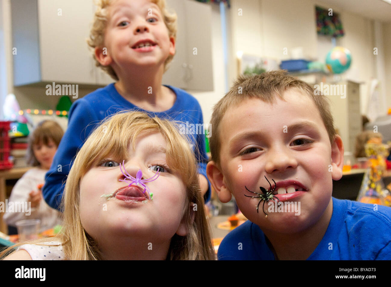 Tre silly kids in aula scolastica mangiare Halloween tratta, giocattolo ragni di plastica Foto Stock