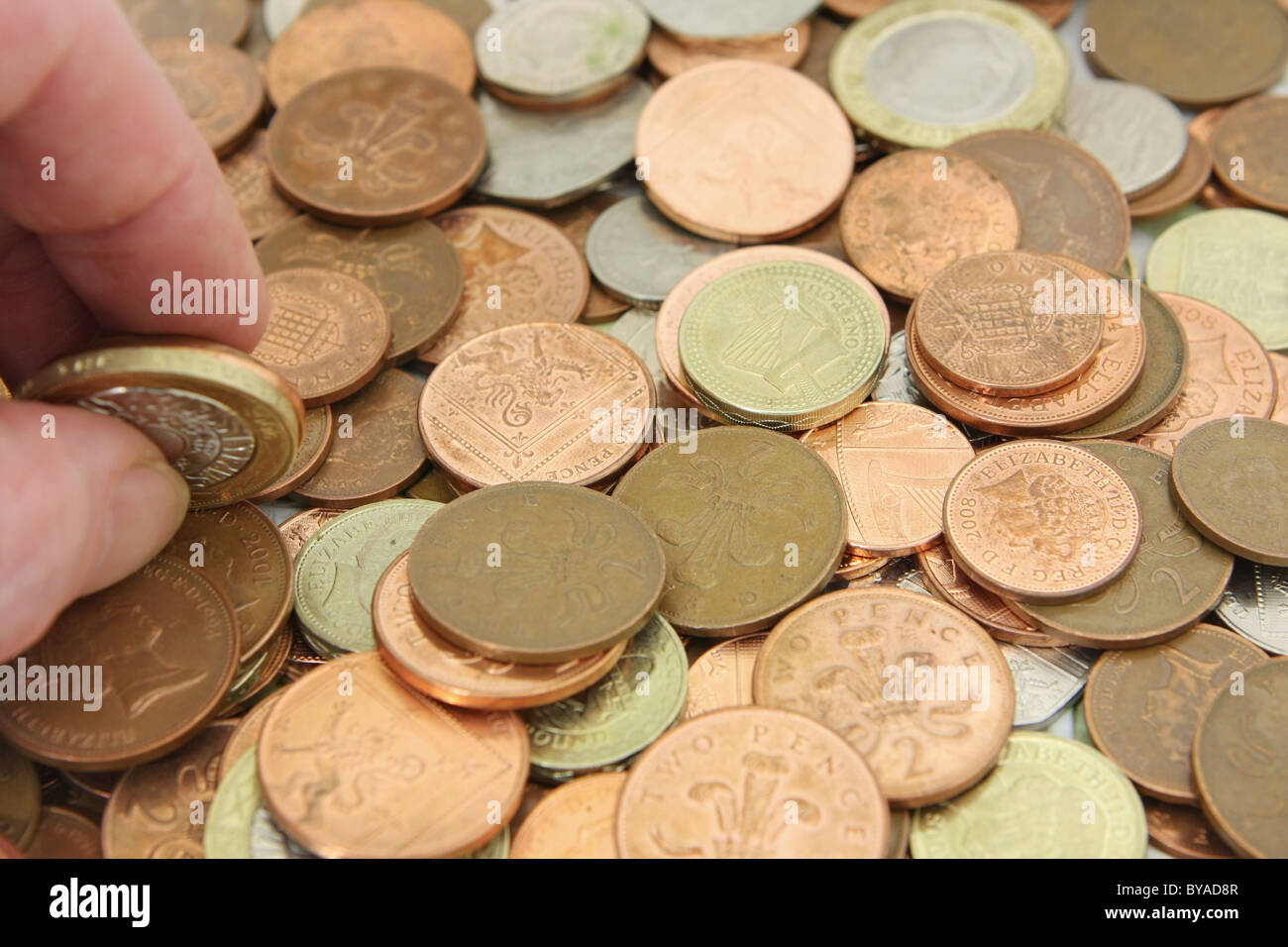 Dito e il pollice tenendo un sterling £2 moneta su una ridda di miste di sterling monete Foto Stock