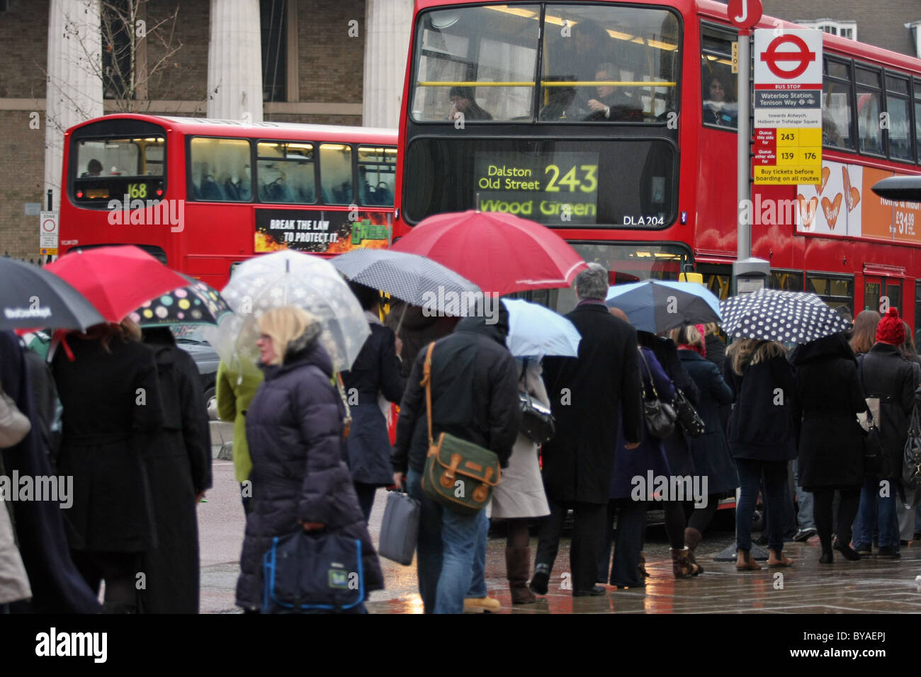 Una coda di persone con ombrelloni fino in attesa di salire a bordo di un rosso di autobus di Londra a Waterloo, Londra Foto Stock