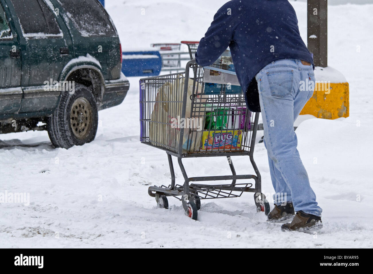 Una shopper le lotte per spingere un carrello dopo una tempesta di neve, Blizzard, che mostra gli effetti del cambiamento climatico. Foto Stock