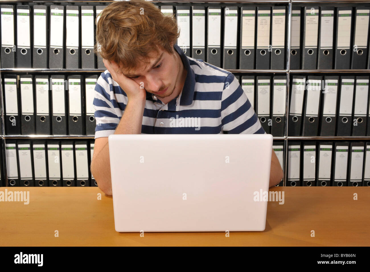 Sottolineato giovane uomo seduto alla scrivania con un notebook Foto Stock