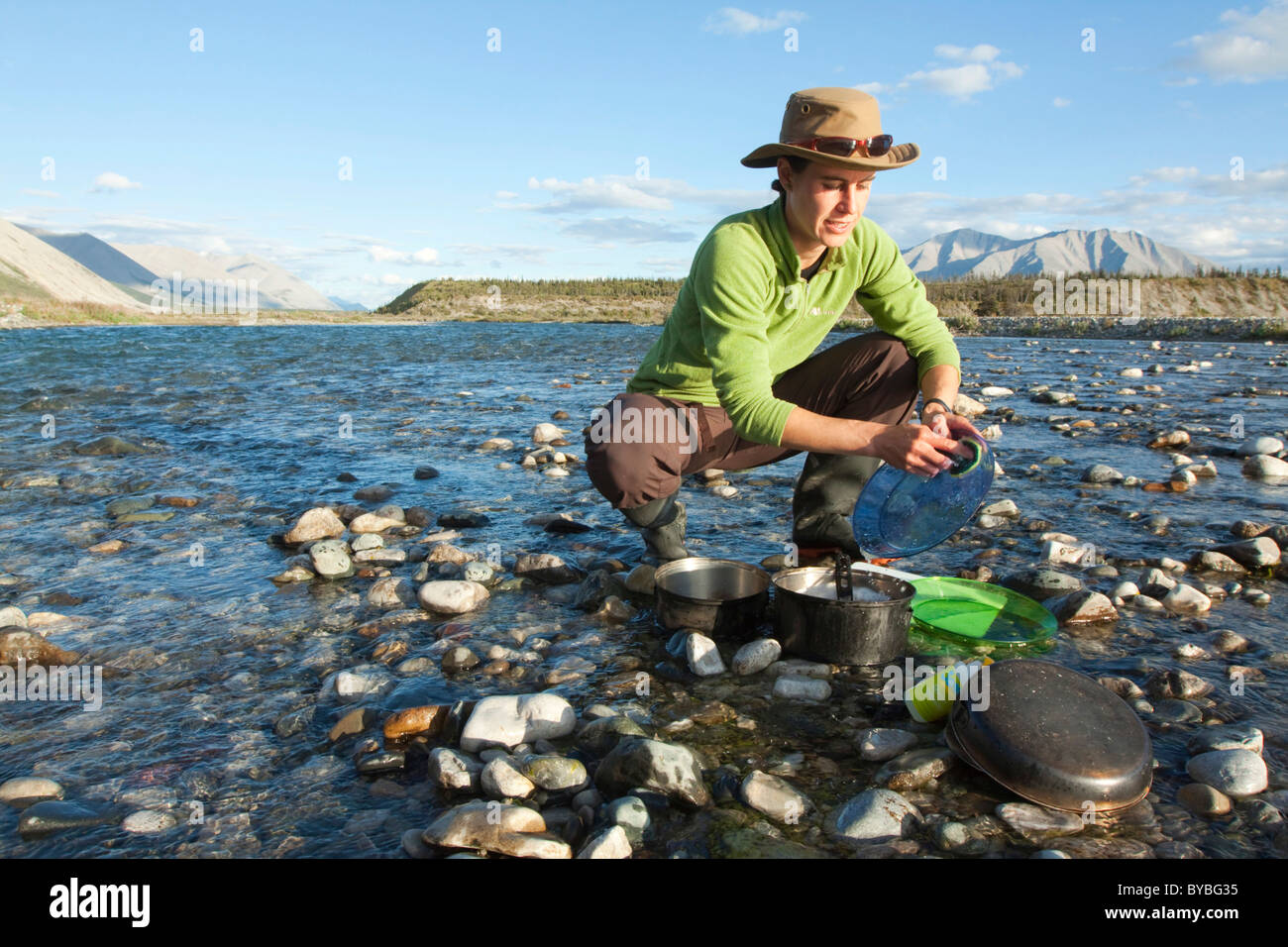Giovane donna lavaggio piatti in un fiume, camping, Mackenzie montagne dietro, Wind River, Yukon Territory, Canada Foto Stock
