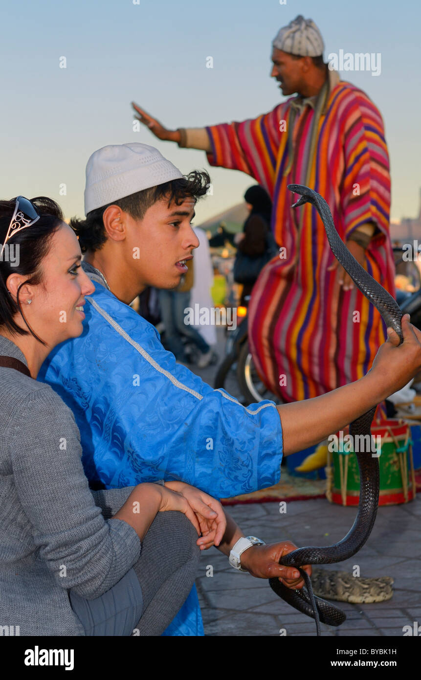 Il serpente incantatore holding cobra nero con bocca aperta con tourist in Piazza Djemaa el Fna a Marrakech Foto Stock