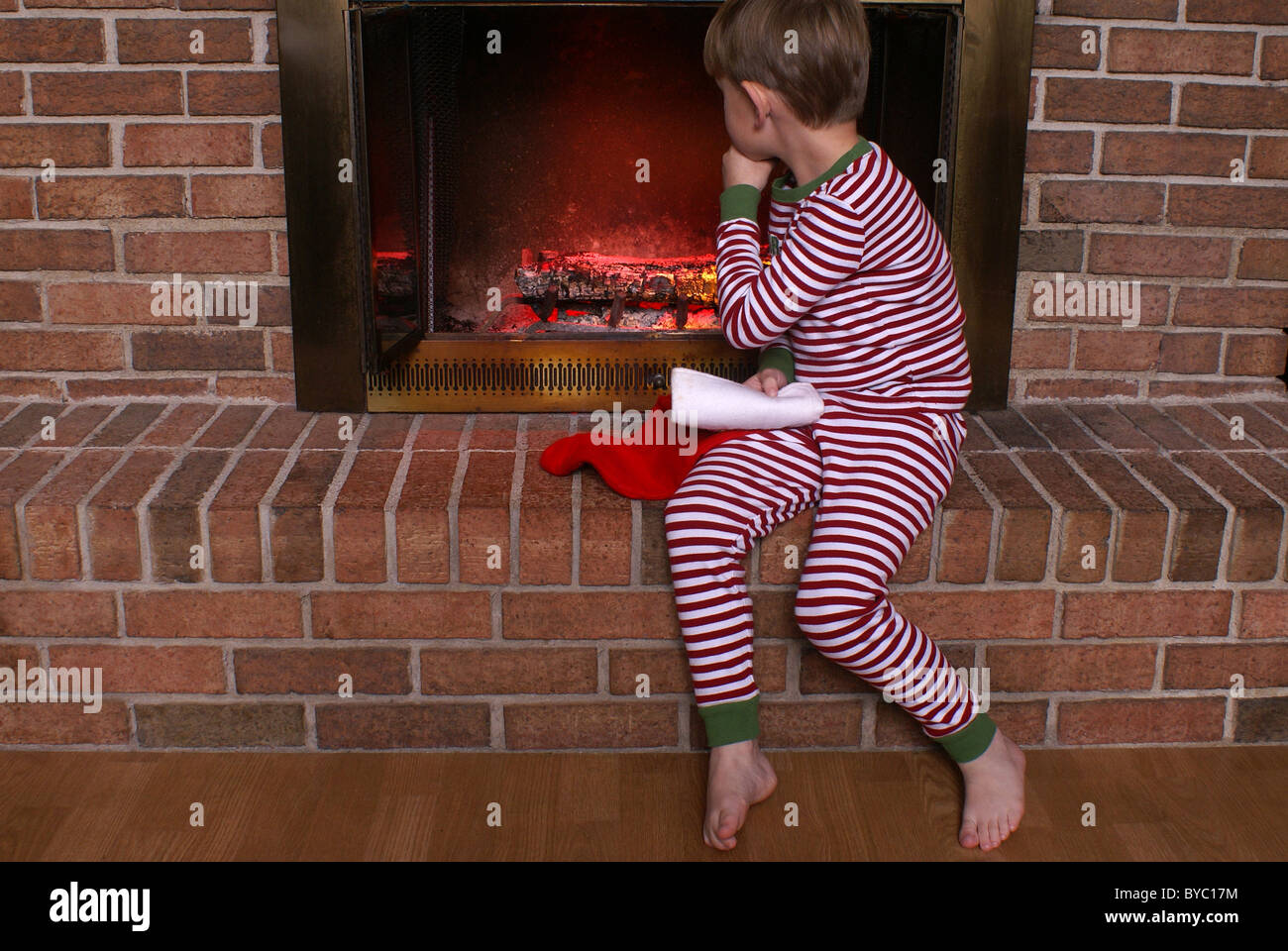 Da seduto e guardando il fuoco nel camino, un ragazzo attende per Santa. Foto Stock