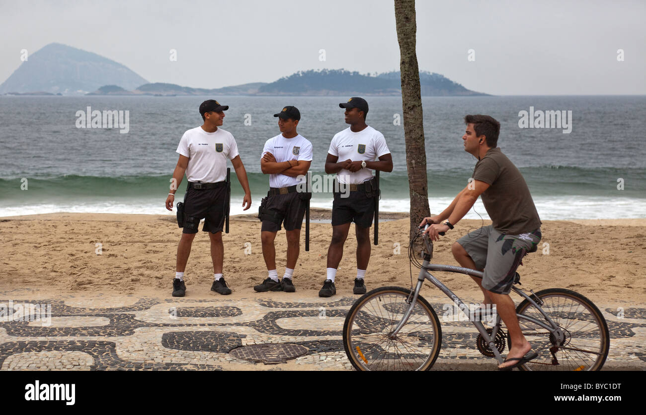 Tre funzionari di polizia sulla spiaggia di Ipanema con uomo passato in bicicletta, a Rio de Janeiro, Brasile, Sud America. Foto Stock
