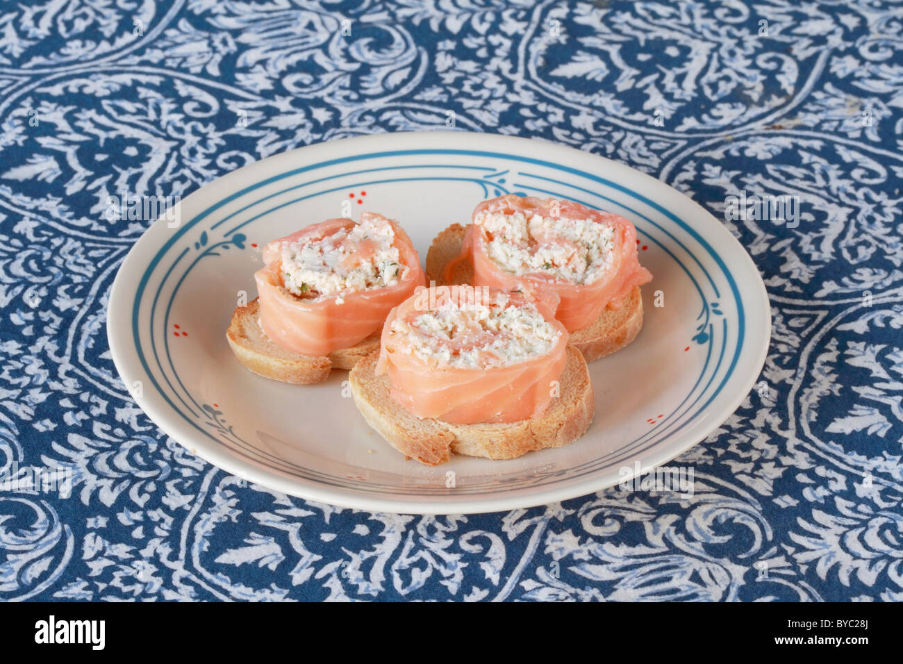 Salmone affumicato arrotolate intorno il formaggio e le erbe ripieno su pane francese tostato antipasti su una piastra Foto Stock