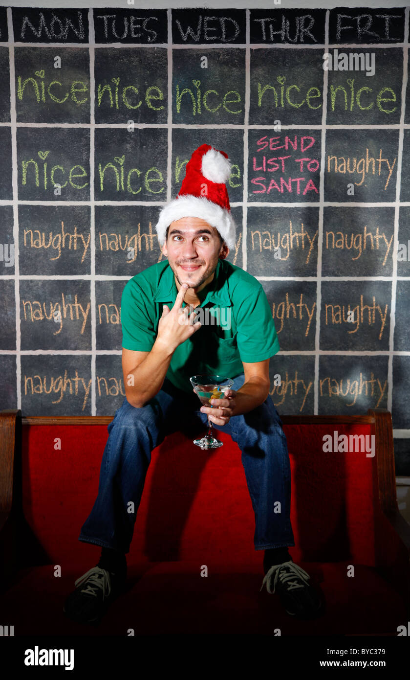 Uomo con elf hat sorridere di fronte naughty e Nizza dicembre Natale calendario con un martini in mano. Foto Stock