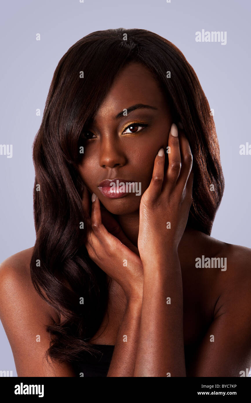 Bella faccia di un attraente nero africano donna con mandorla occhi e lunghi capelli ondulati e le mani nel suo volto, isolata. Foto Stock