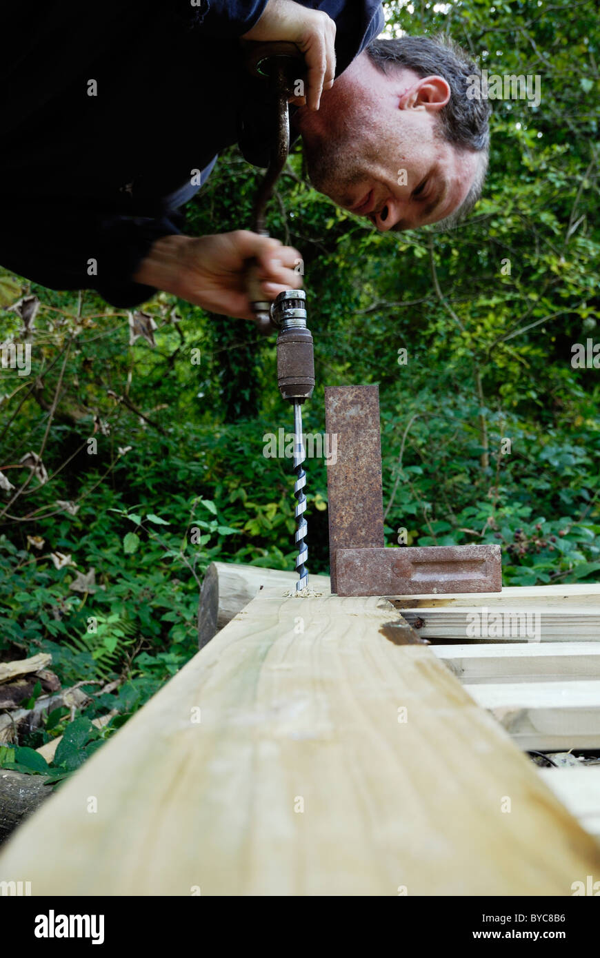 Uomo di legname di foratura utilizzando un tutore e bit con un set square utilizzato come una guida, Galles Foto Stock
