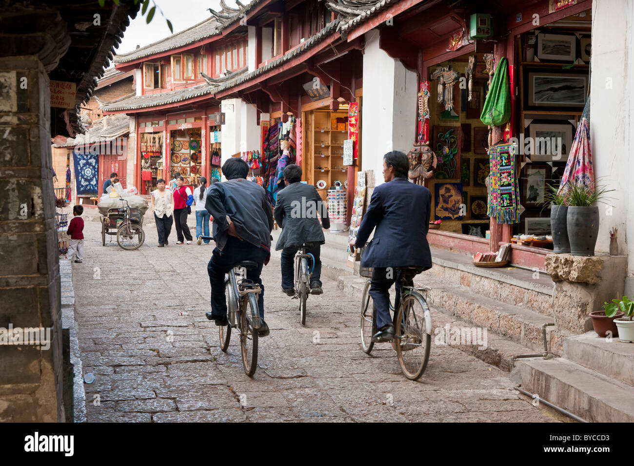 Tre uomini in bicicletta attraverso una stretta corsia pavimentata a Lijiang old town, nella provincia dello Yunnan in Cina. JMH4755 Foto Stock