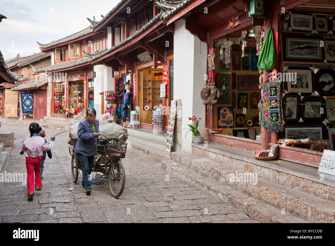 Donna con il triciclo che trasportano merci in uno stretto vicolo lastricato a Lijiang old town, nella provincia dello Yunnan in Cina. JMH4756 Foto Stock