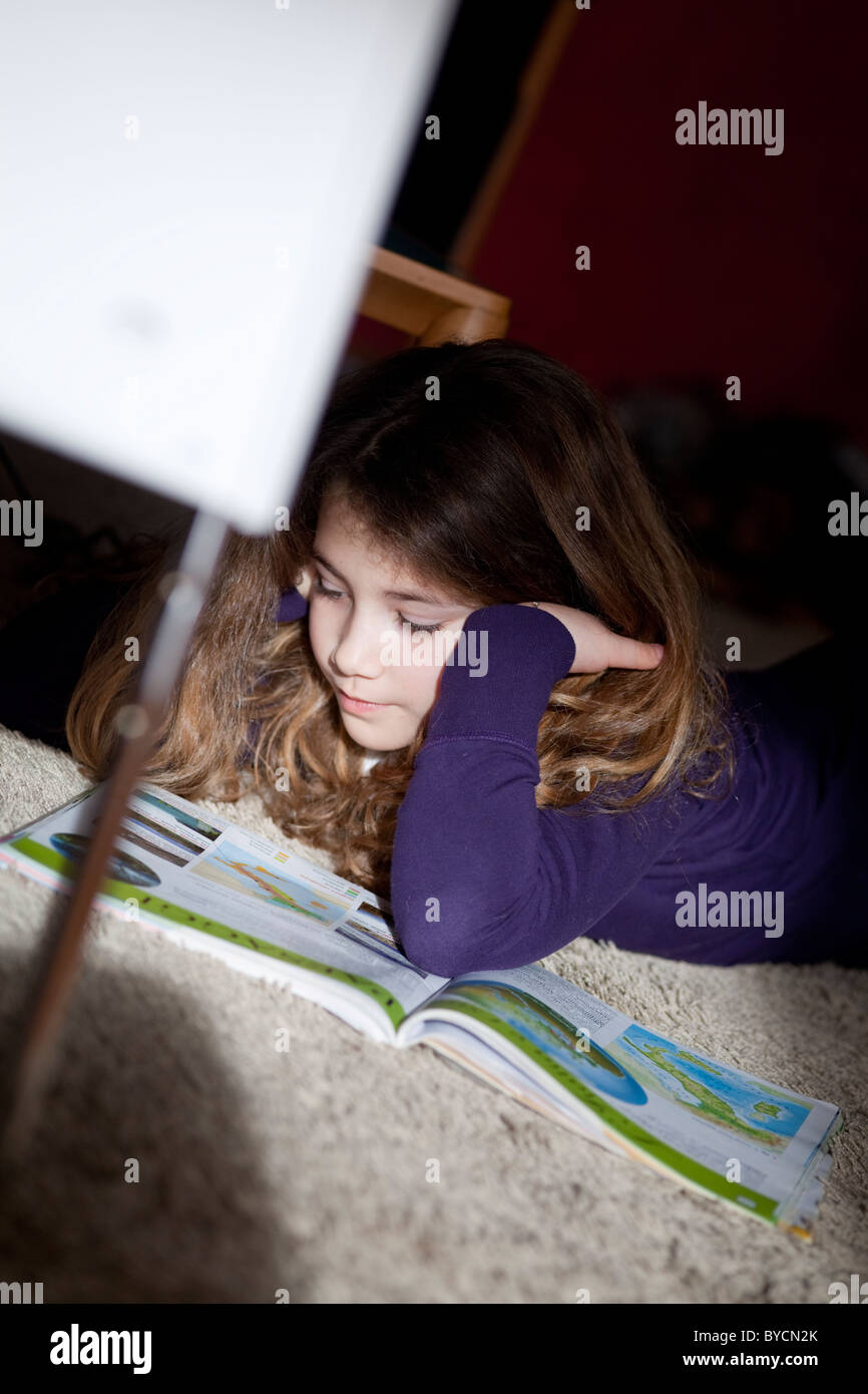 Giovani schoolgirl geografia di apprendimento da un libro di testo a casa la posa sul tappeto Foto Stock