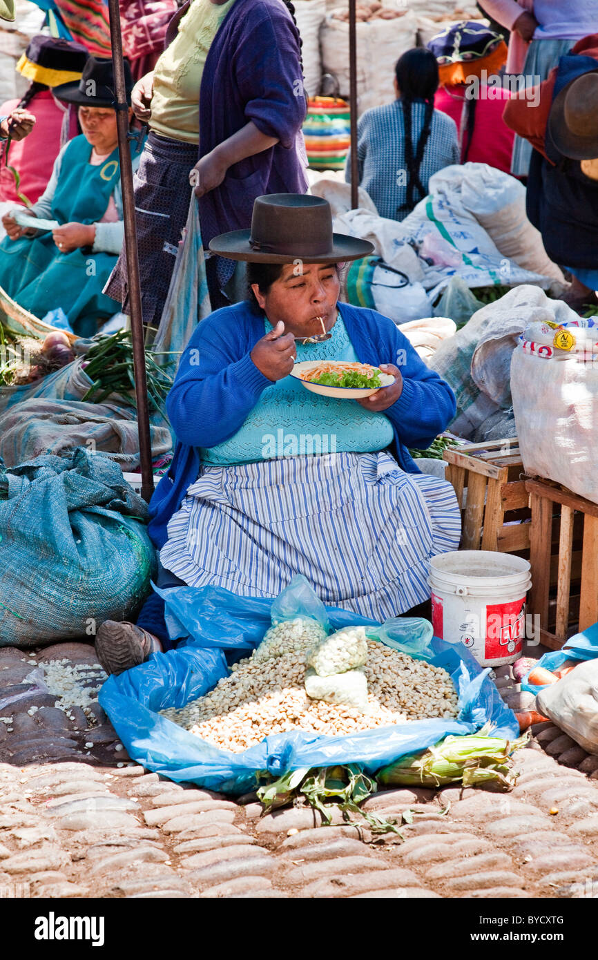 Signora anziana sat mangiare in luogo di mercato a Pisac, Valle Sacra, Perù, Sud America. Foto Stock