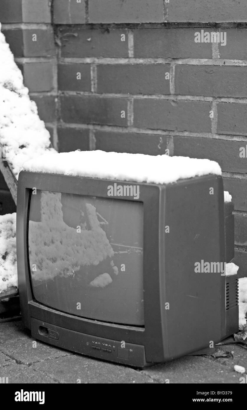 Un vecchio televisore portatile su una stradina innevata, gettate per rottami di fronte a un muro di mattoni. Foto Stock