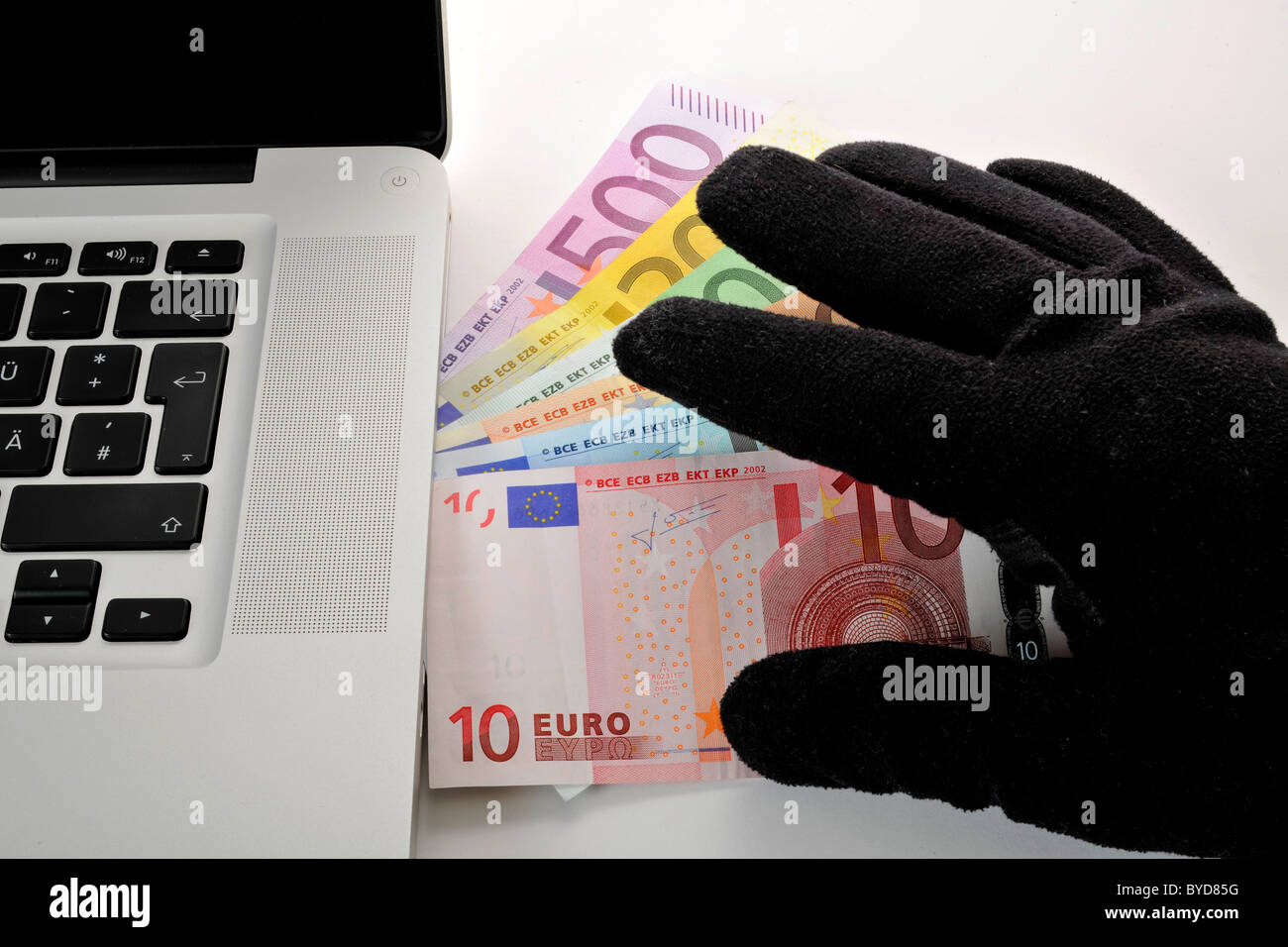 Laptop e PC e una mano in un guanto nero al di sopra di un ventilatore di varie banconote in euro, immagine simbolica per illegale di Internet per le aziende Foto Stock