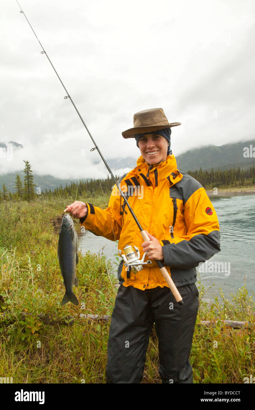 Giovane donna pesca, presentando la sua cattura, grandi Arctic temolo (Thymallus arcticus), Wind River, Yukon Territory, Canada Foto Stock