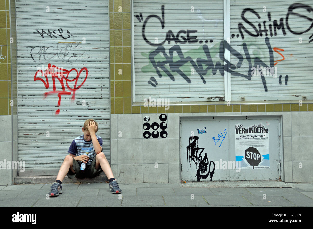 Lonely bambino di nove anni nella parte anteriore della chiusura di un business che è cosparso di graffiti, Germania, Europa Foto Stock