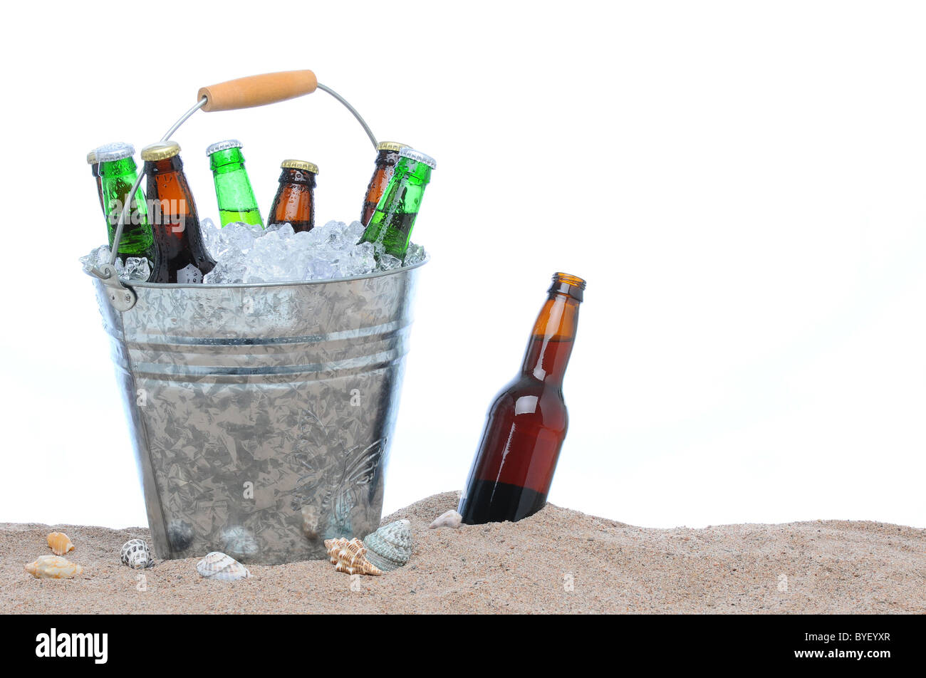Un assortimento di bottiglie di birra in un secchio di ghiaccio nella sabbia isolata su bianco. Foto Stock