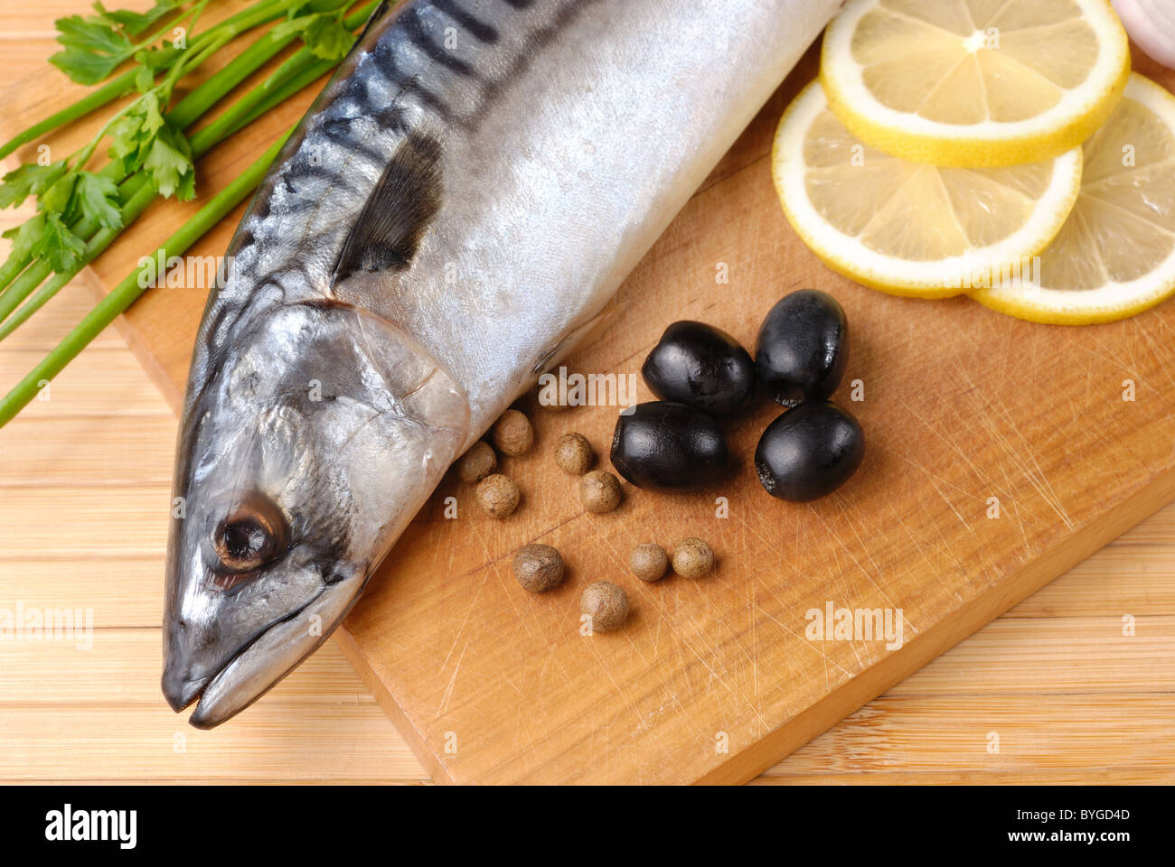 Sgombri freschi con olive, limoni e cipolle su tagliere di legno Foto Stock